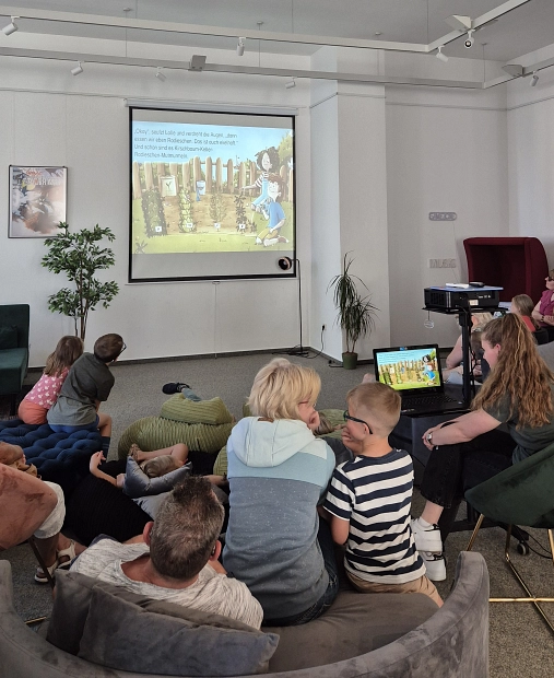 Foto eines Bilderbuchkinos. Zu sehen sind Kinder von hinten, die auf eine Leinwand schauen.